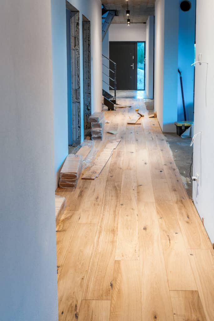 Installation Parquet Bois: Rénovation Couloir Moderne Couloir en rénovation avec parquet en bois clair en cours d'installation. Des piles de planches neuves et des outils sont visibles.